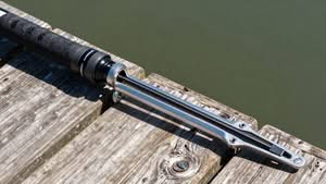 A fishing rod with a metal gimbal butt rests on a wooden dock above the water.